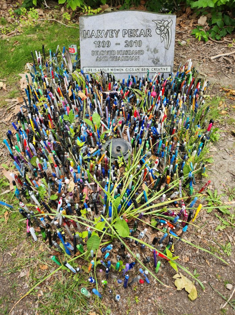 Grave of Harvey Pekar, comic book, graphic novel, and movie script writer and actor, with all different types of writing utensils stuck into the ground around it. Located in the Lake View Cemetery.