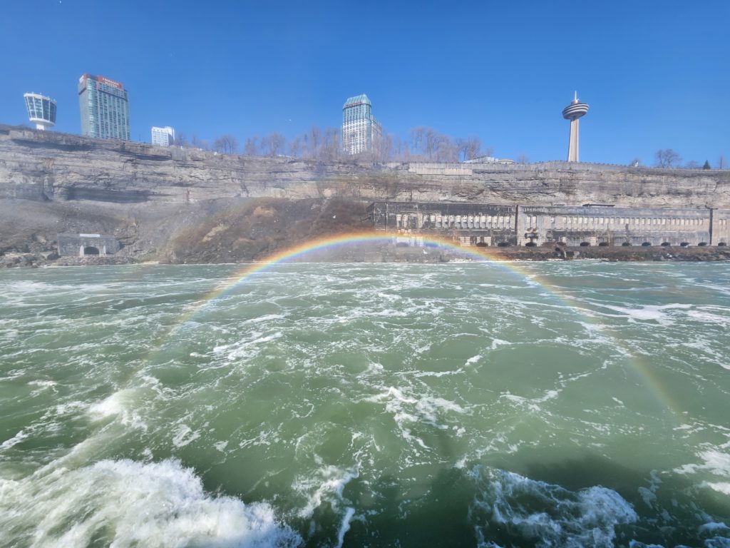 A view of the Canadian hotels at Niagara Falls from a boat. A rainbow is created because of the mist from the falls. 