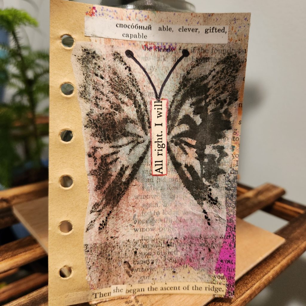 Mixed media artwork with a butterfly covering the majority of the page. Different colors are sprinkled around it. The words able, clever, gifted, and capable are on a piece of dictionary paper at the top. The words "all right, I will" create the butterfly's body. At the bottom it reads, "Then she began the ascent of the ridge." This page was day 2 in my "I am" project. I am capable.