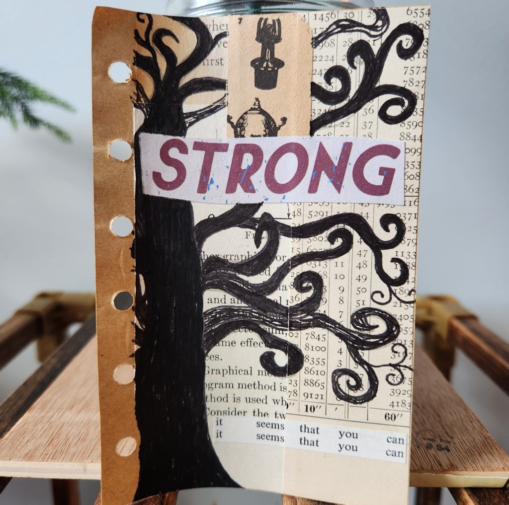 A mixed media art page that has random book pages as the background. On the background pages, in black marker, is a hand drawn tree. The word "strong" is across the middle of the page.