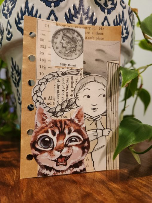 A mixed media art page with the words "silly head" on a picture of a coin. Near the center is a line drawn picture of a girl with long pigtails peeking around the corner with a mischievous look on her face. Beside her is a sticker of a cat making a funny face. The background is made up of random book pages.