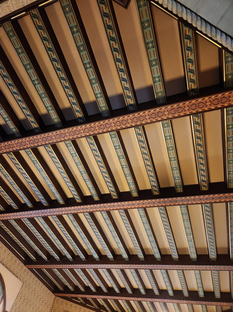 A ceiling made up of wooden beams that are painted with an elaborate design. 