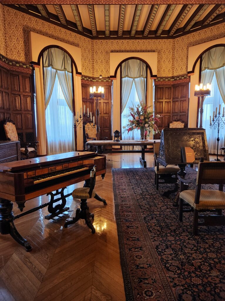 The music room at the Biltmore Estate. A small antique piano sits to the left, with chairs and a table scattered throughout the room so people can sit and listen to music being played. 