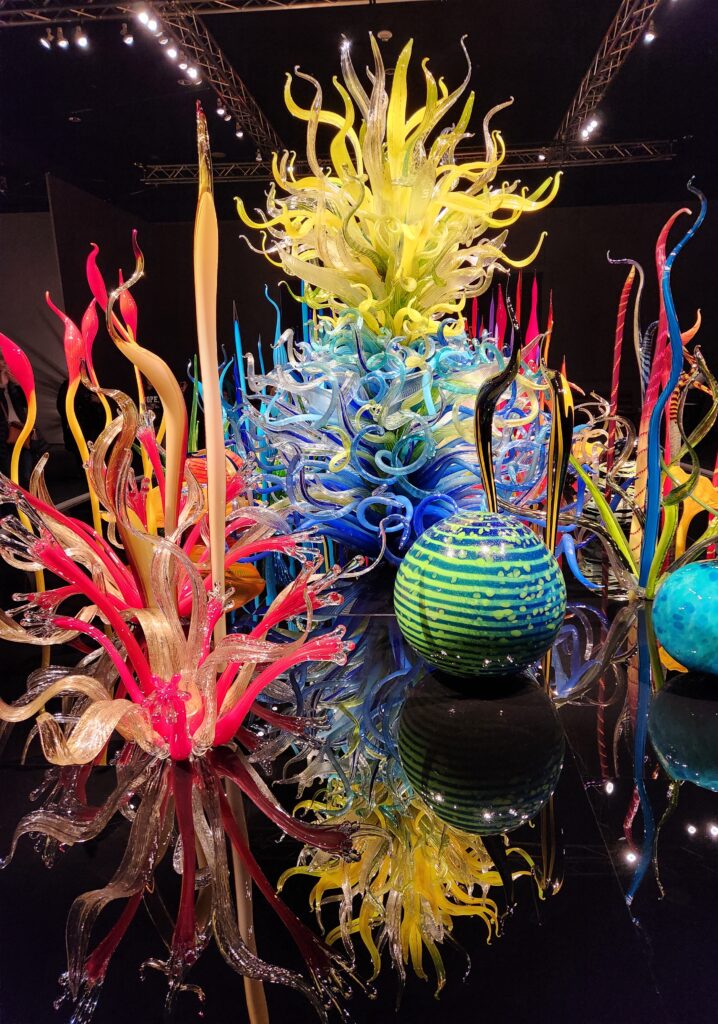 Chihuly at Biltmore glass art installation. Several different pieces of Chihuly's glass art, placed onto a large oval base that makes it look like the pieces are sitting in water and being reflected back up.  